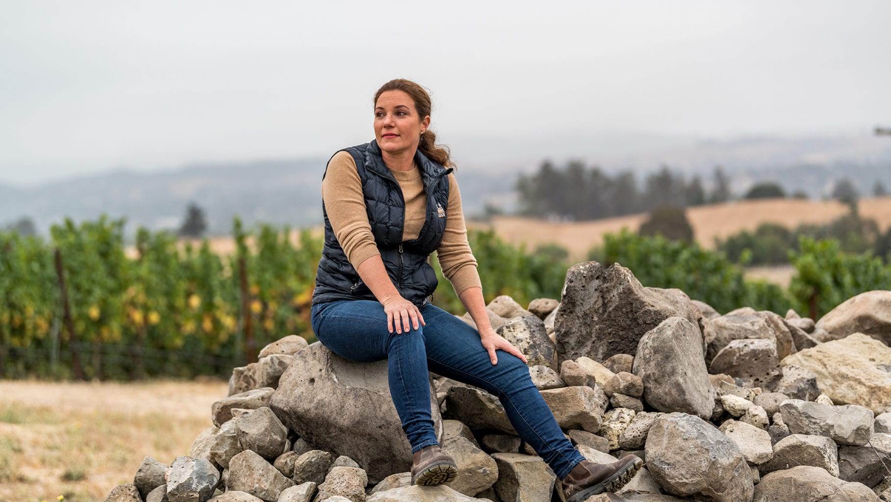 Winemaker Megan Baccitich seated on basalt stones beside the estate vineyard